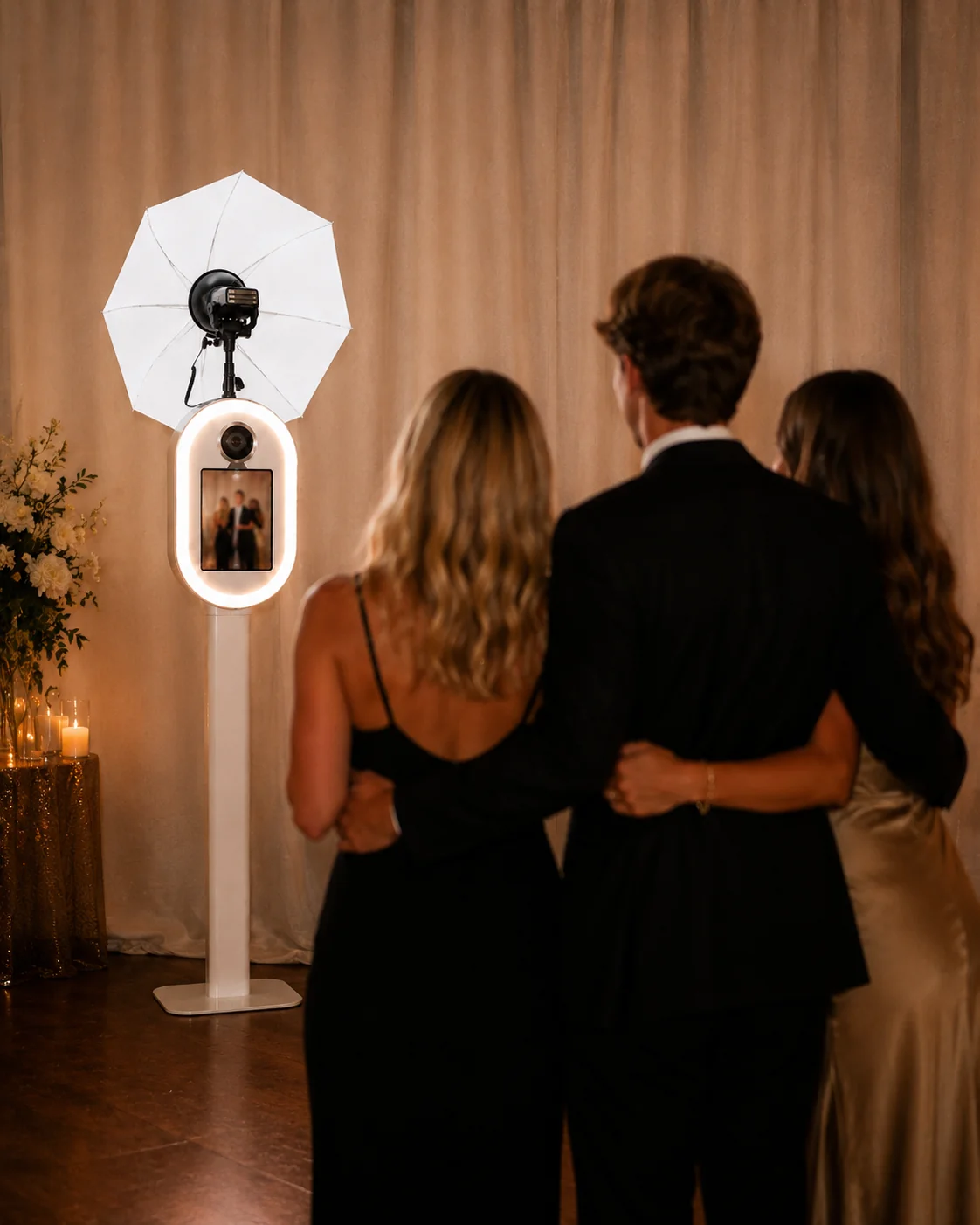 Drie gasten in avondkleding klaar voor hun foto met de Pro Photobooth tijdens een chique avond-event met champagnegoud gordijn en kaarslicht